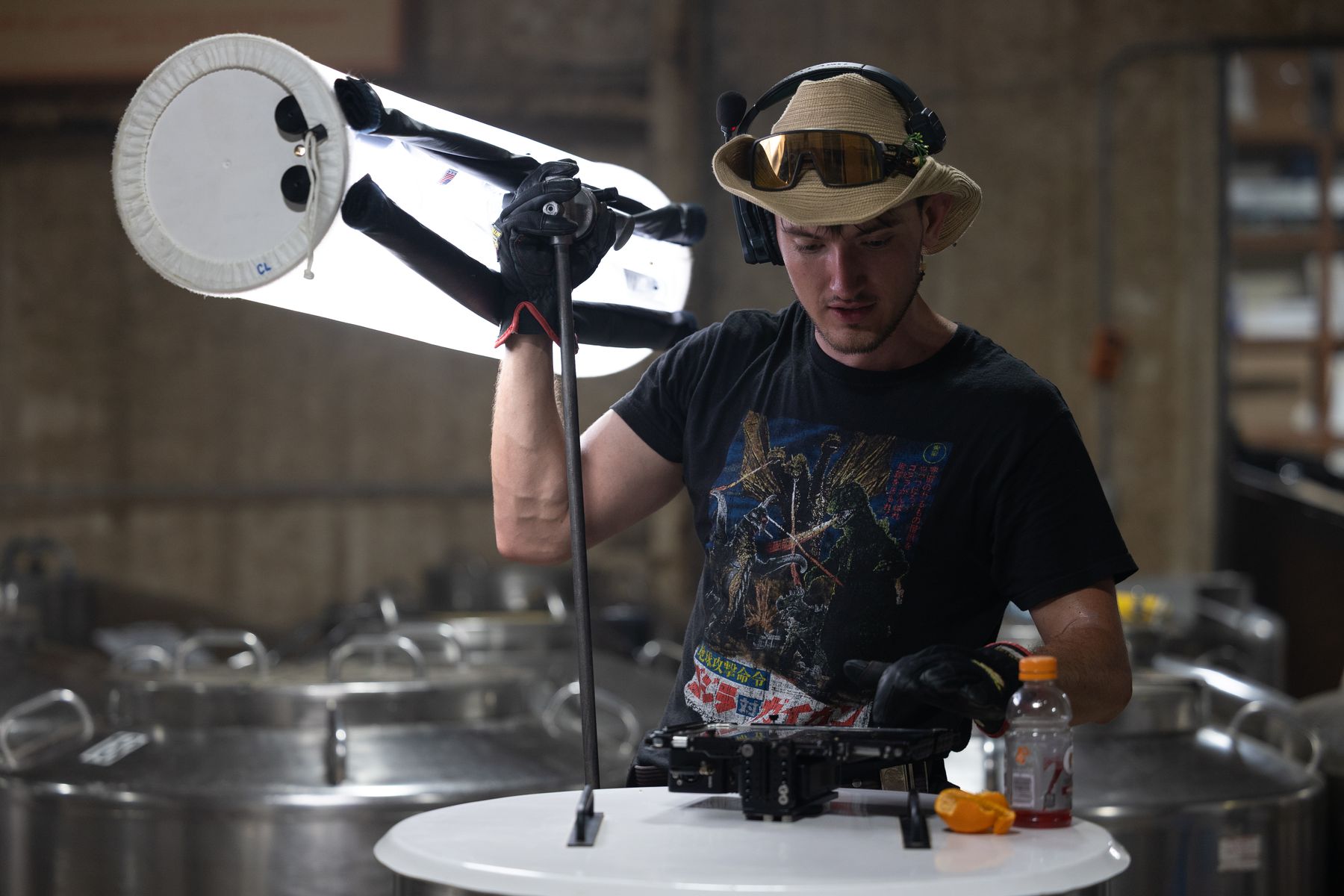 Gaffer rigging a large softbox above stainless tanks on an interior set