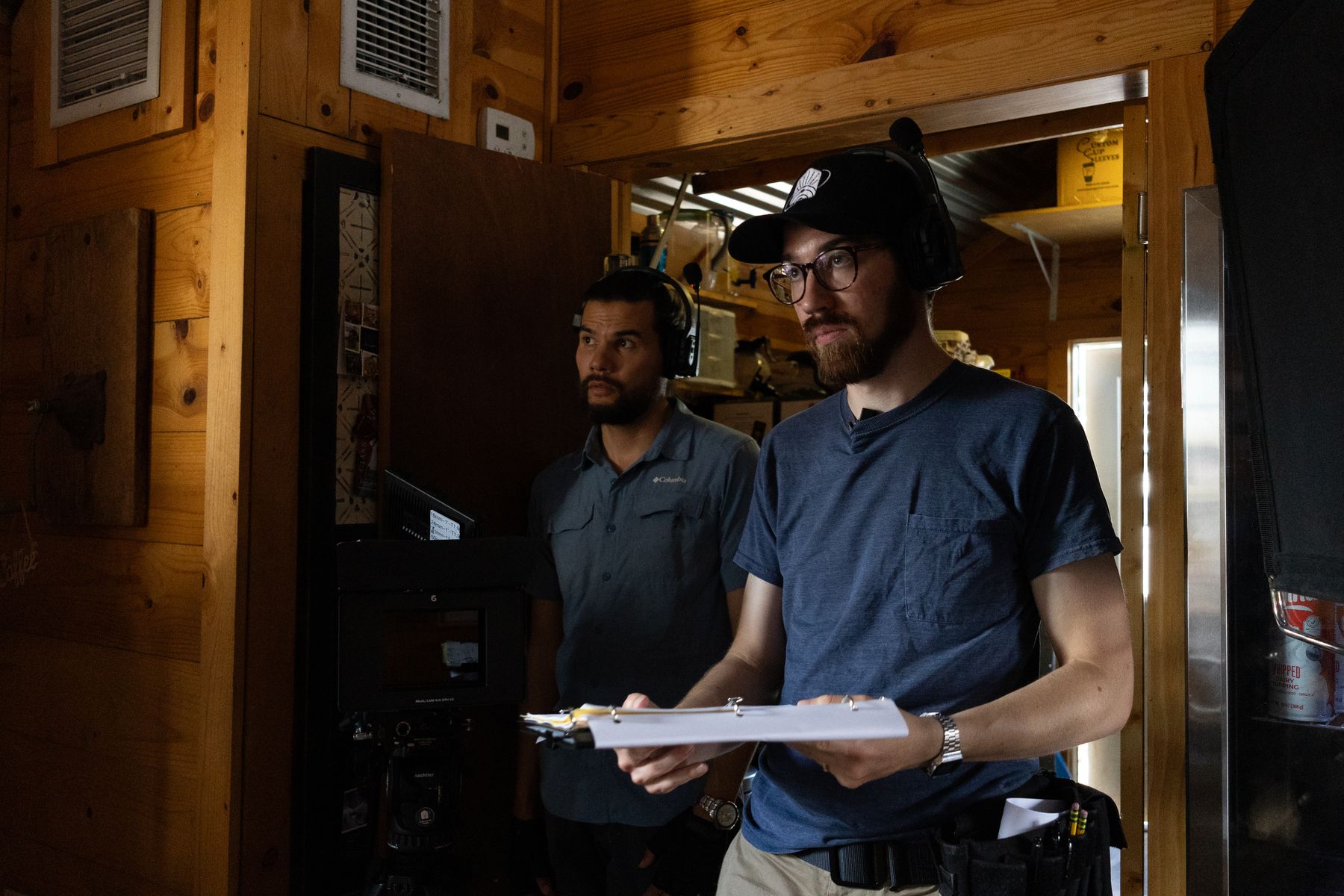 Crew with a slate and headsets inside a wood-panelled set between takes