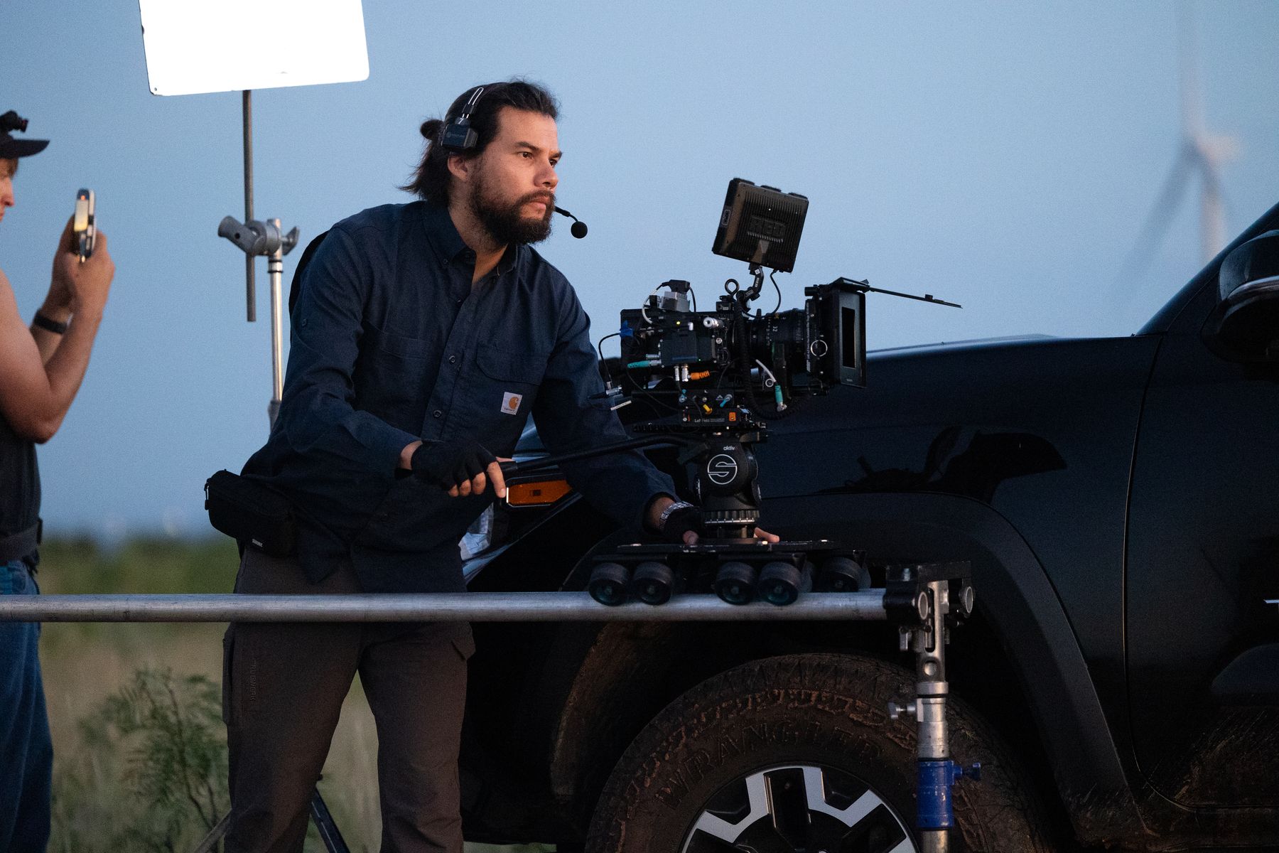 Camera operator behind a rig mounted to a truck under open sky