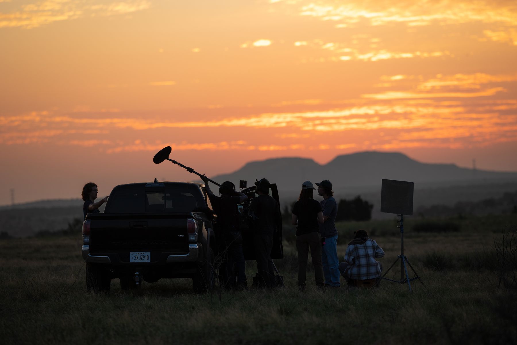 Crew and a pickup silhouetted against a mesa at sunset